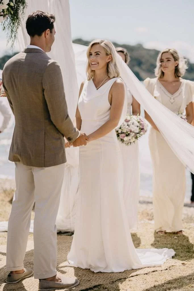 Bride and groom holding hands on a beach, bride in a Trish Peng V-neck gown
